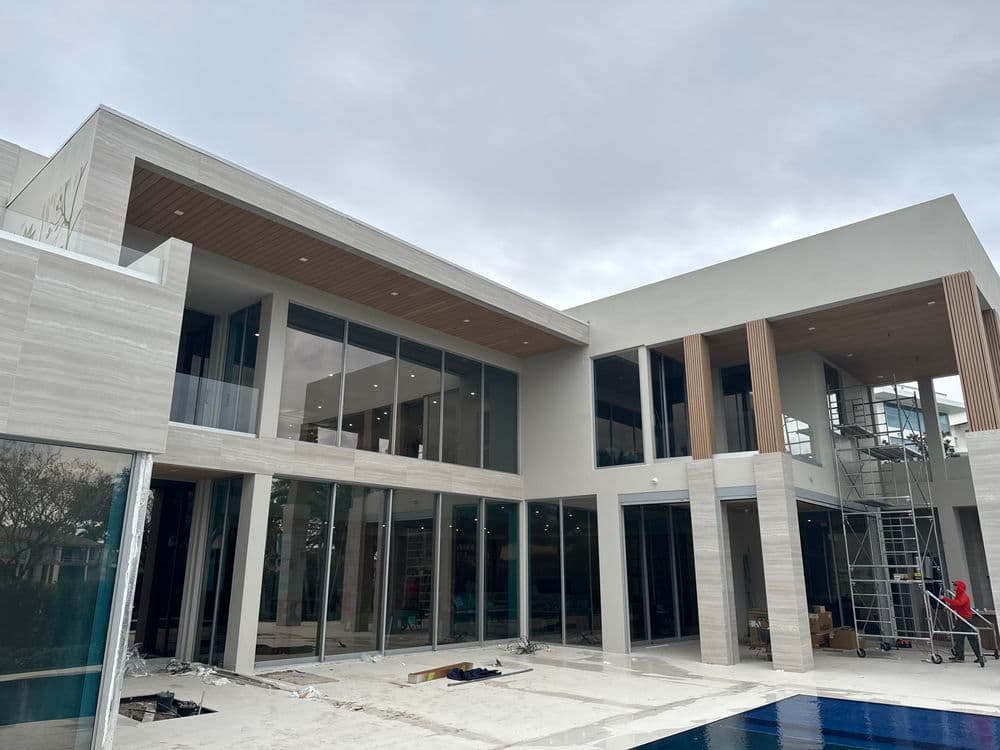 Modern luxury home under construction with large glass windows and a pool.