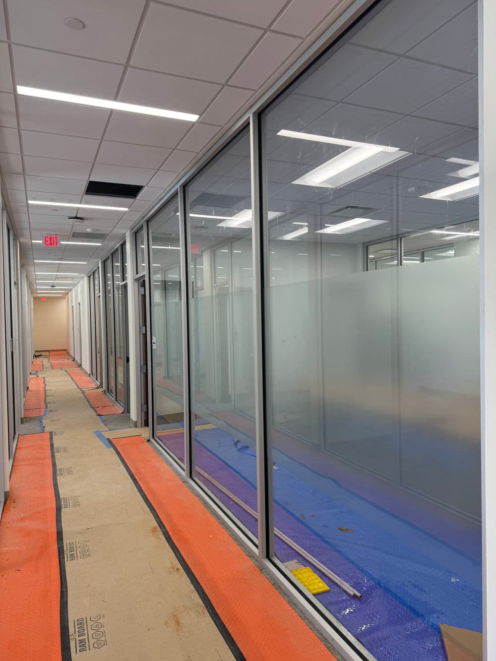 Modern office corridor with frosted glass meeting rooms and construction flooring.